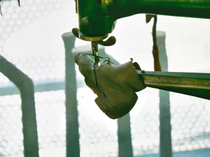 Nahaufnahme der Nähmaschine im Betrieb - ein Kinderschuh wird unter der Nadel der grünen ADLER-Maschine bearbeitet, Detail des Nähvorgangs mit Maschinenkopf und Lederverarbeitung.