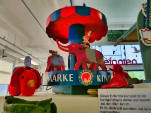 Historisches elektrisches Elefanten-Karussell der Marke "Elefanten" aus den 1960er Jahren im Schuhmuseum - ein handgefertigtes Kinderspielzeug mit rot-blauen Elefanten und Markenschriftzug, das als Museumsstück ausgestellt ist.