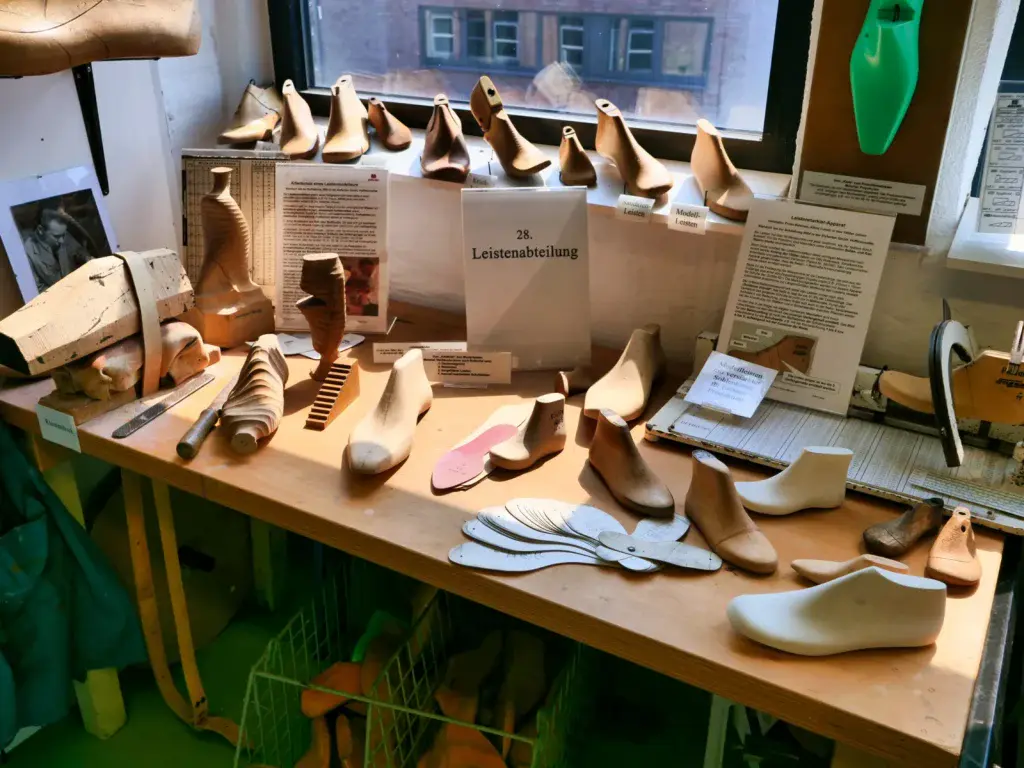 Ausstellungstisch mit Schuhleisten aus Holz und verschiedenen Werkzeugen der Schuhmacherei, darunter die Station "28. Leistenabteilung" mit Informationstafeln zur handwerklichen Schuhfertigung.
