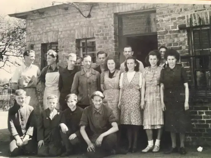 Historisches Gruppenfoto der Belegschaft einer Schuhfabrik vor einem Backsteingebäude, aufgenommen in den 1940er oder 1950er Jahren.