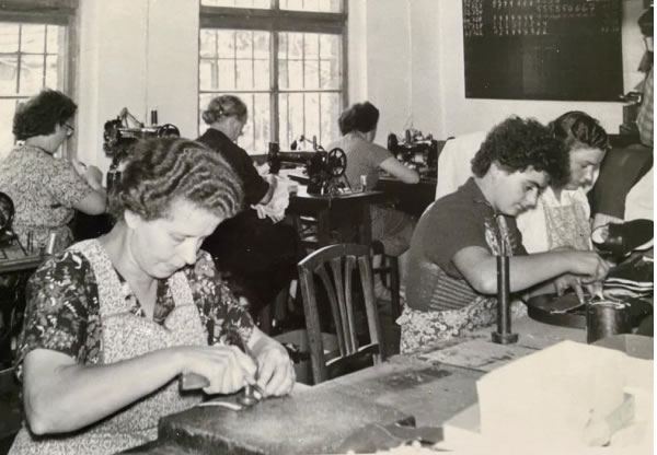 Historische Schwarz-Weiß-Aufnahme aus einer Schuhfabrik mit Arbeiterinnen an Nähmaschinen in handwerklicher Produktion