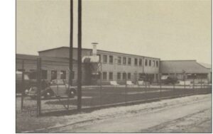 Historisches Schwarz-Weiß-Foto eines Industriegebäudes mit langer Fassade und Schornstein, eine Fabrik aus der Nachkriegszeit.