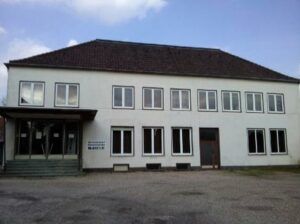 Weißes zweigeschossiges Fabrik- oder Verwaltungsgebäude mit Walmdach und symmetrischer Fensterfassade,