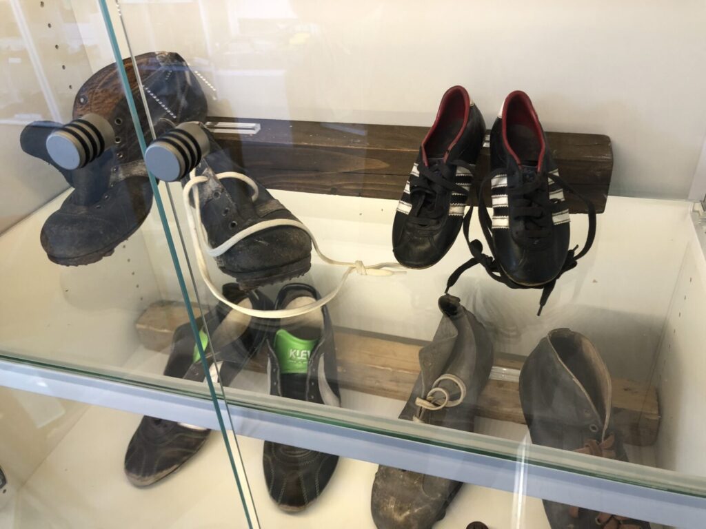 Das Bild zeigt eine Vitrine mit historischen Fußballschuhen in einer Museumsausstellung.