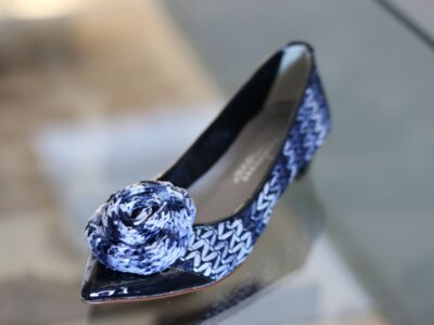 Das Bild zeigt einen eleganten Damenpumps mit spitz zulaufender Schuhspitze, aufwändigem blauen Flechtmuster sowie einer kunstvoll gearbeiteten Blütenapplikation an der Vorderseite.
