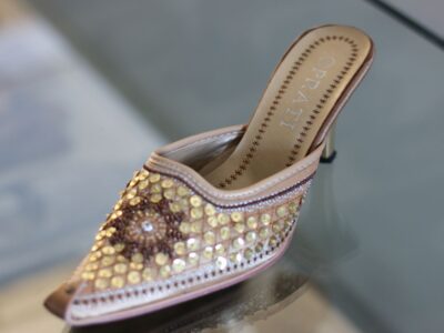 Das Bild zeigt einen eleganten Damenschuh (Mule/Slipper) mit offener Ferse und spitzer Form, der aufwendig mit goldfarbenen Pailletten und Perlen sowie floralen Mustern dekoriert ist. Die Marke „PRATI“ ist im Futter zu sehen.